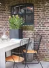 A table and chairs set on a patio next to a brick wall with a window. Produktbild-Vorschau