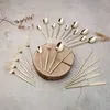 A collection of gold-colored cutlery arranged on a textured surface with a wooden disc. Anteprima dell’immagine prodotto