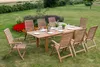 A wooden garden dining set with a table and chairs set up on a lawn, surrounded by flowers and greenery. Náhled obrázku produktu
