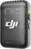 A close-up studio shot of a black DJI Mic 2 transmitter with a transparent casing, revealing internal circuitry. The product is angled slightly, showing its side buttons and a green indicator light. Náhled obrázku produktu