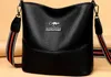 A black leather handbag with a decorative strap is shown against a light beige background. Náhľad obrázku produktu