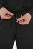 A close-up of a person's hands tying a drawstring on black pants. Produktbild-Vorschau