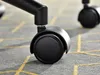 A close-up shot of a black office chair caster wheel on a patterned carpet. Voir les images du produit