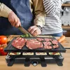A person is preparing food on a raclette grill, with raw meat and vegetables on the grill surface and cheese in the small pans below. Produktbild-Vorschau