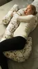 A woman is sleeping on a bed, hugging a large U-shaped pillow. Podgląd zdjęcia produktu