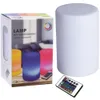 A product shot of a white cylindrical LED lamp with its remote control, next to its packaging. Produktbild-Vorschau