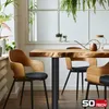 A dining table with wooden chairs in a bright, plant-filled room with a large window. Produktbild-Vorschau