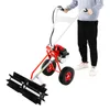 A person is holding a red and black gas-powered sweeper machine with black brushes on a white background. Produktbild-Vorschau