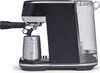 A black and silver espresso machine with a clear water tank and a metal milk frothing pitcher. Produktbild-Vorschau