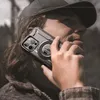 A person wearing a cap and jacket is holding an iPhone with a protective case to their ear, as if making a call. Produktbild-Vorschau