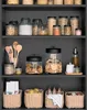 A dark gray shelf unit filled with various glass jars and woven baskets containing food items and kitchen utensils. Náhled obrázku produktu