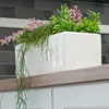 A white ceramic planter with artificial plants sits on a wooden shelf above white cabinets. The background is a tiled wall. Produktbild-Vorschau