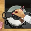 A person's hand is shown closing the lid of a pressure cooker on a stovetop. Podgląd zdjęcia produktu