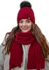 A woman wearing a red knitted hat with a black pom-pom and a matching red scarf. Voir les images du produit