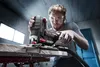 A man is using a cordless jigsaw to cut a piece of wood in a workshop. Produktbild-Vorschau