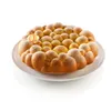 A round cake with a bubbly texture, dusted with powdered sugar, sits on a white plate against a white background. Anteprima dell’immagine prodotto