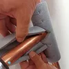 Hands are shown installing a copper pipe into a grey foam insulation fitting. Produktbild-Vorschau