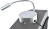 A close-up of a silver bedside lamp with a USB port and a switch, attached to a gray upholstered headboard. Náhled obrázku produktu