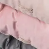 A close-up view of two fabric items, likely blankets or cushions, in pink and beige colors, with small leather tags attached. Náhled obrázku produktu
