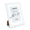 A white picture frame is shown at an angle against a white background. The frame has a white mat and a printed insert with text and a logo. Anteprima dell’immagine prodotto