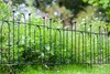 A black metal garden fence bordering a lush green garden with flowers in the background. Podgląd zdjęcia produktu