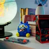 A blue monster toy sits on a shelf next to a globe, books, and a miniature arcade machine. Voir les images du produit