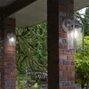 Two outdoor wall lights mounted on brick pillars, with lush greenery and flowers in the background. Voir les images du produit