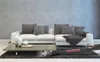 A modern living room with a white sectional sofa, a coffee table with decorative vases and a book, and a gray rug. A cordless vacuum cleaner is on the rug. Produktbild-Vorschau