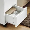 A close-up view of an open drawer of a white rolling cabinet, revealing a pair of white headphones and a brown notebook inside. Náhľad obrázku produktu