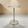 A stainless steel bar table with a round top and base, set against a light wood paneled wall and a concrete floor. Produktbild-Vorschau