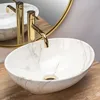 A marble-patterned sink with gold faucets sits on a wooden countertop, reflected in a gold-rimmed mirror. Produktbild-Vorschau