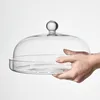 A hand is holding a glass cake stand with a lid. Náhľad obrázku produktu