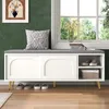 A white shoe bench with a gray cushion is placed in a hallway next to a window. Shoes are stored underneath and on shelves within the bench. A decorative pillow sits on the cushion. Produktbild-Vorschau