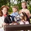 Three young girls are sitting on a bench outdoors, each holding a hobby horse. Anteprima dell’immagine prodotto