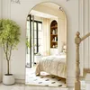 A full-length arched mirror reflects a bedroom interior, showing a bed, nightstand, and bookshelf. A potted plant is in the foreground. Anteprima dell’immagine prodotto
