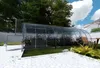 A greenhouse in a backyard setting with a table and chair nearby. Podgląd zdjęcia produktu