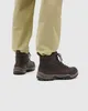 A close-up shot of a person's legs wearing brown lace-up boots and khaki pants. Produktbild-Vorschau