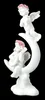 A white figurine of two cherubs playing musical instruments while sitting on a crescent moon, set against a black background. Produktbild-Vorschau