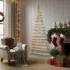 A cozy living room decorated for Christmas, featuring a wall-mounted Christmas tree made of wood and lights, a plaid armchair with blankets, and a fireplace with stockings and gifts. Podgląd zdjęcia produktu