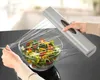 A person is using a plastic wrap dispenser to cover a bowl of salad. Produktbild-Vorschau