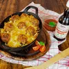 A dish of meatballs baked with cheese, served with a bottle of Worcester sauce and cherry tomatoes. Produktbild-Vorschau