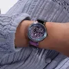 A close-up shot of a woman's wrist wearing a colorful Guess watch, with her arm resting on a textured purple fabric. Náhled obrázku produktu