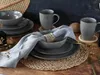 A table setting with stoneware plates, bowls, and mugs, arranged on a woven placemat. Náhľad obrázku produktu
