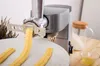 A kitchen machine with a pasta maker attachment is extruding pasta onto a white plate. Ingredients like flour and egg are visible in the background. Podgląd zdjęcia produktu
