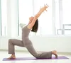 A woman is doing yoga on a mat in front of a large window. Produktbild-Vorschau