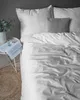 A neatly made bed with white striped satin bedding and a gray pillow. Produktbild-Vorschau