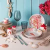 A collection of coral-themed tableware and decorative items arranged on a white surface against a light blue wooden background. Voir les images du produit
