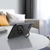 A black smartphone with a ring holder attached is placed on a white table in a living room setting. Náhled obrázku produktu