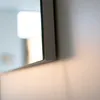 A close-up shot of the edge of a mirror frame mounted on a wall, with soft lighting. Anteprima dell’immagine prodotto