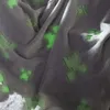A close-up view of a soft, gray blanket with a repeating pattern of glowing green Minecraft creeper faces. Podgląd zdjęcia produktu
